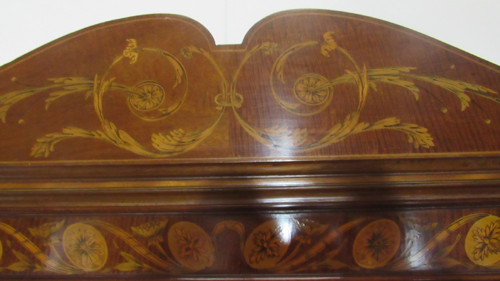 An antique mahogany glazed display cabinet featuring marquetry inlay, two glass doors, four small drawers, and square tapered legs. View III