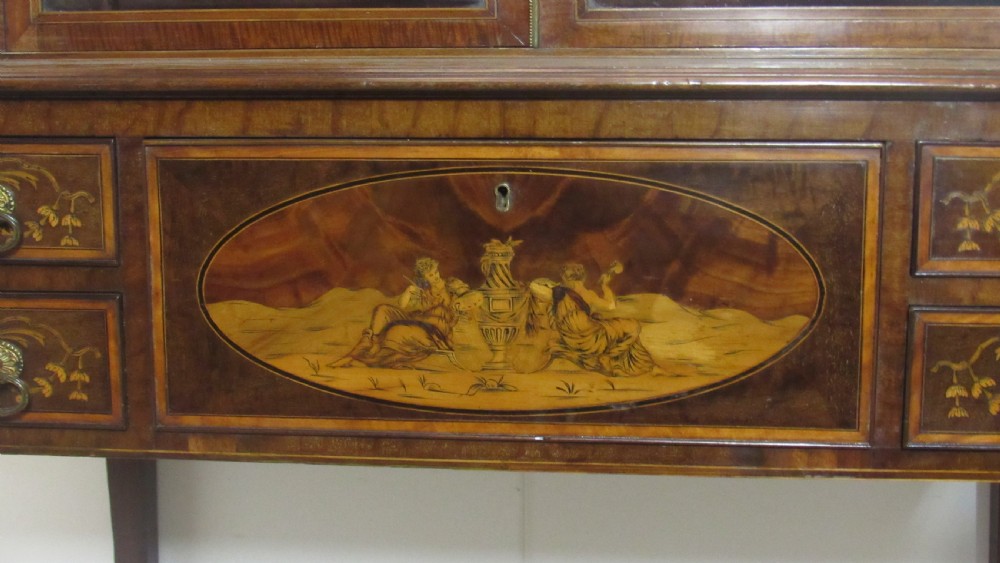 An antique mahogany glazed display cabinet featuring marquetry inlay, two glass doors, four small drawers, and square tapered legs. View VII