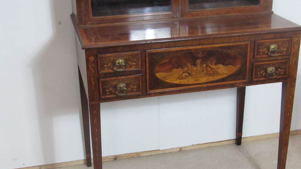 An antique mahogany glazed display cabinet featuring marquetry inlay, two glass doors, four small drawers, and square tapered legs. View XI