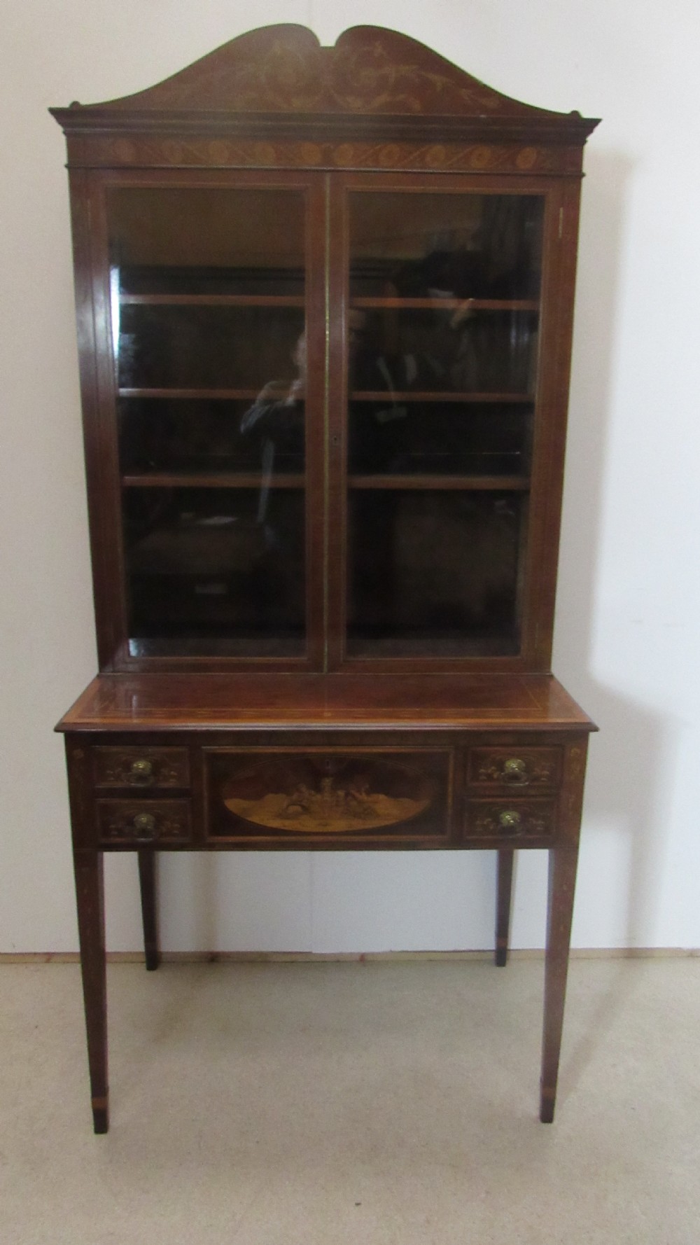 An antique mahogany glazed display cabinet featuring marquetry inlay, two glass doors, four small drawers, and square tapered legs. View XII