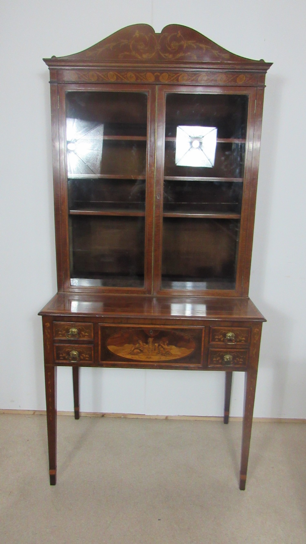 An antique mahogany glazed display cabinet featuring marquetry inlay, two glass doors, four small drawers, and square tapered legs. View XIII