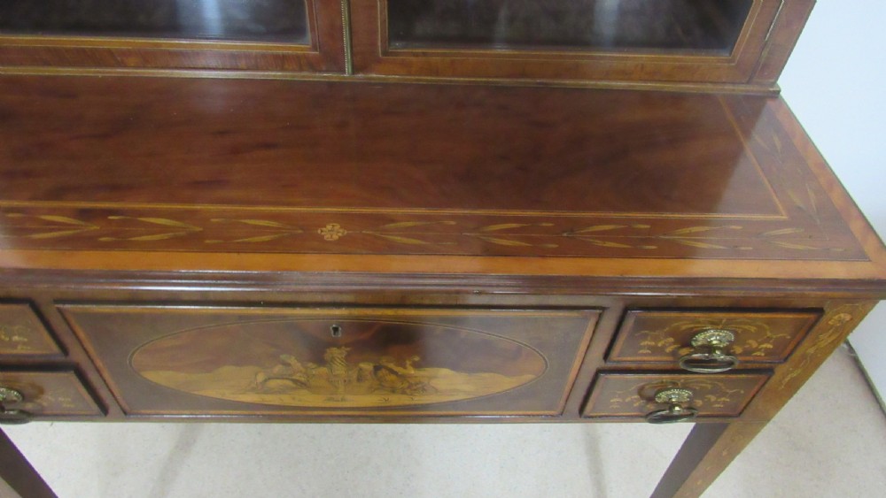 An antique mahogany glazed display cabinet featuring marquetry inlay, two glass doors, four small drawers, and square tapered legs. View XV