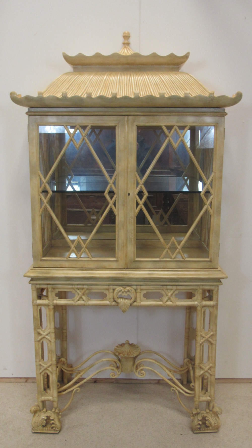 A cream painted Chinoiserie display cabinet on a stand featuring a pagoda-style roof, diamond lattice glass doors, and faux bamboo detailing.