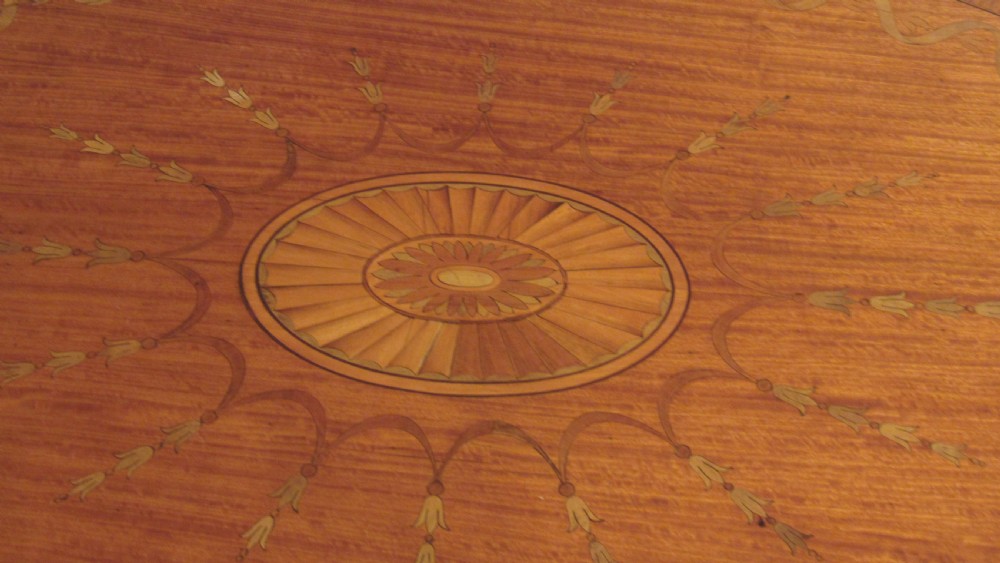 An oval antique satinwood occasional table featuring decorative marquetry inlay on top, tapered legs, and a small lower shelf with a brass gallery rail. View V