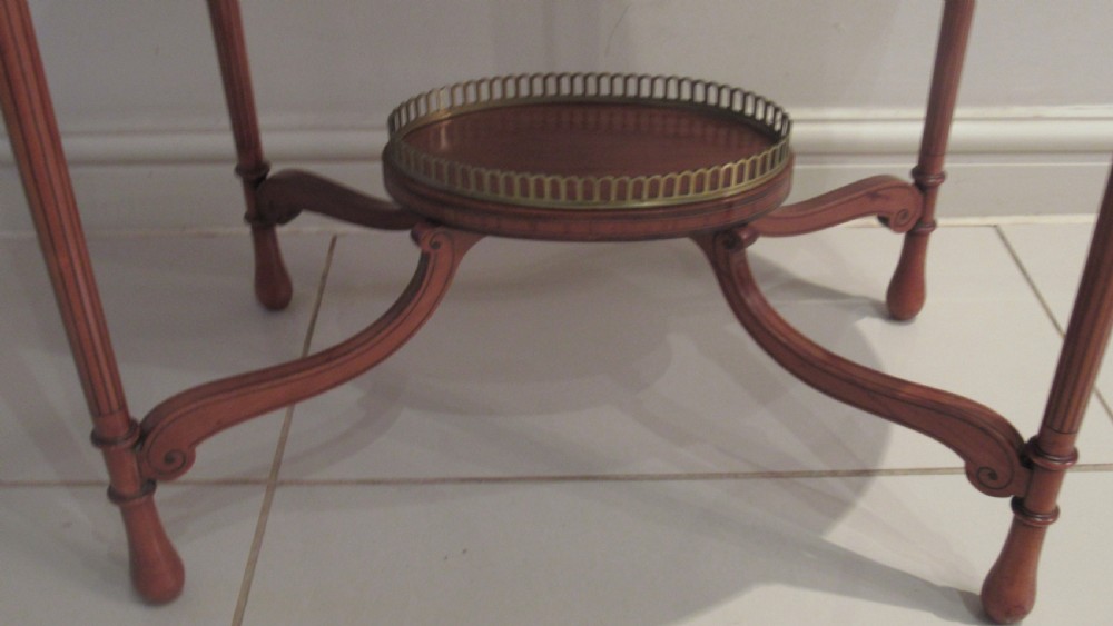 An oval antique satinwood occasional table featuring decorative marquetry inlay on top, tapered legs, and a small lower shelf with a brass gallery rail. View VII
