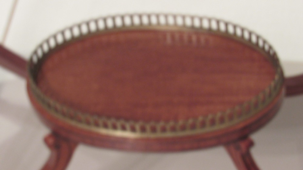 An oval antique satinwood occasional table featuring decorative marquetry inlay on top, tapered legs, and a small lower shelf with a brass gallery rail. View XVII
