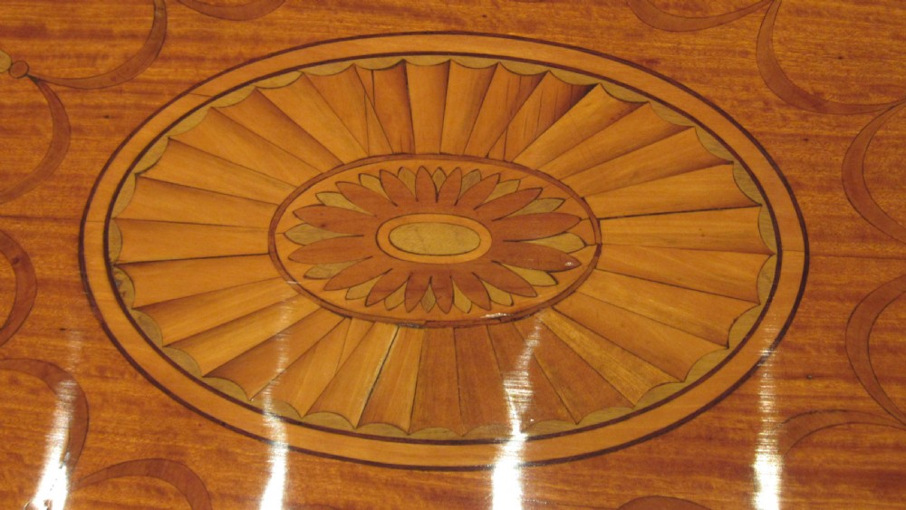 An oval antique satinwood occasional table featuring decorative marquetry inlay on top, tapered legs, and a small lower shelf with a brass gallery rail. View XVIII