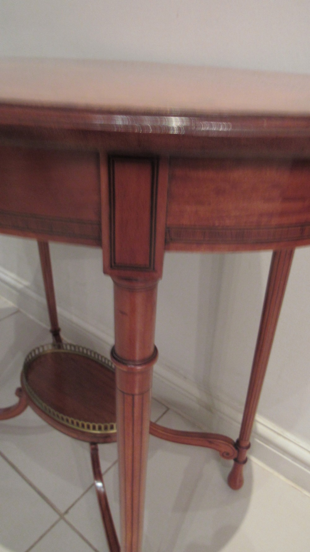 An oval antique satinwood occasional table featuring decorative marquetry inlay on top, tapered legs, and a small lower shelf with a brass gallery rail. View XXI