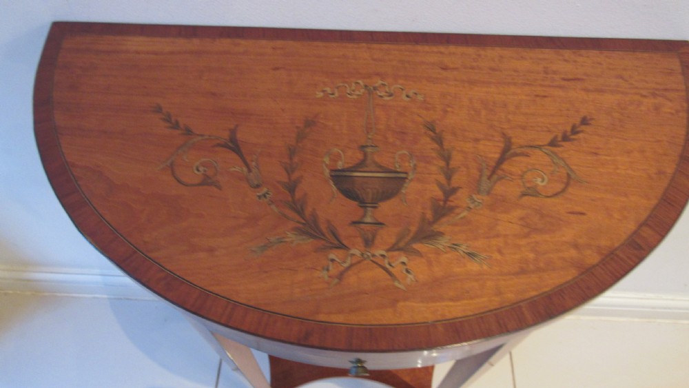 A semi-circular golden satinwood demilune console table featuring urn marquetry inlay, slender tapered legs, and an under-tier shelf. View III