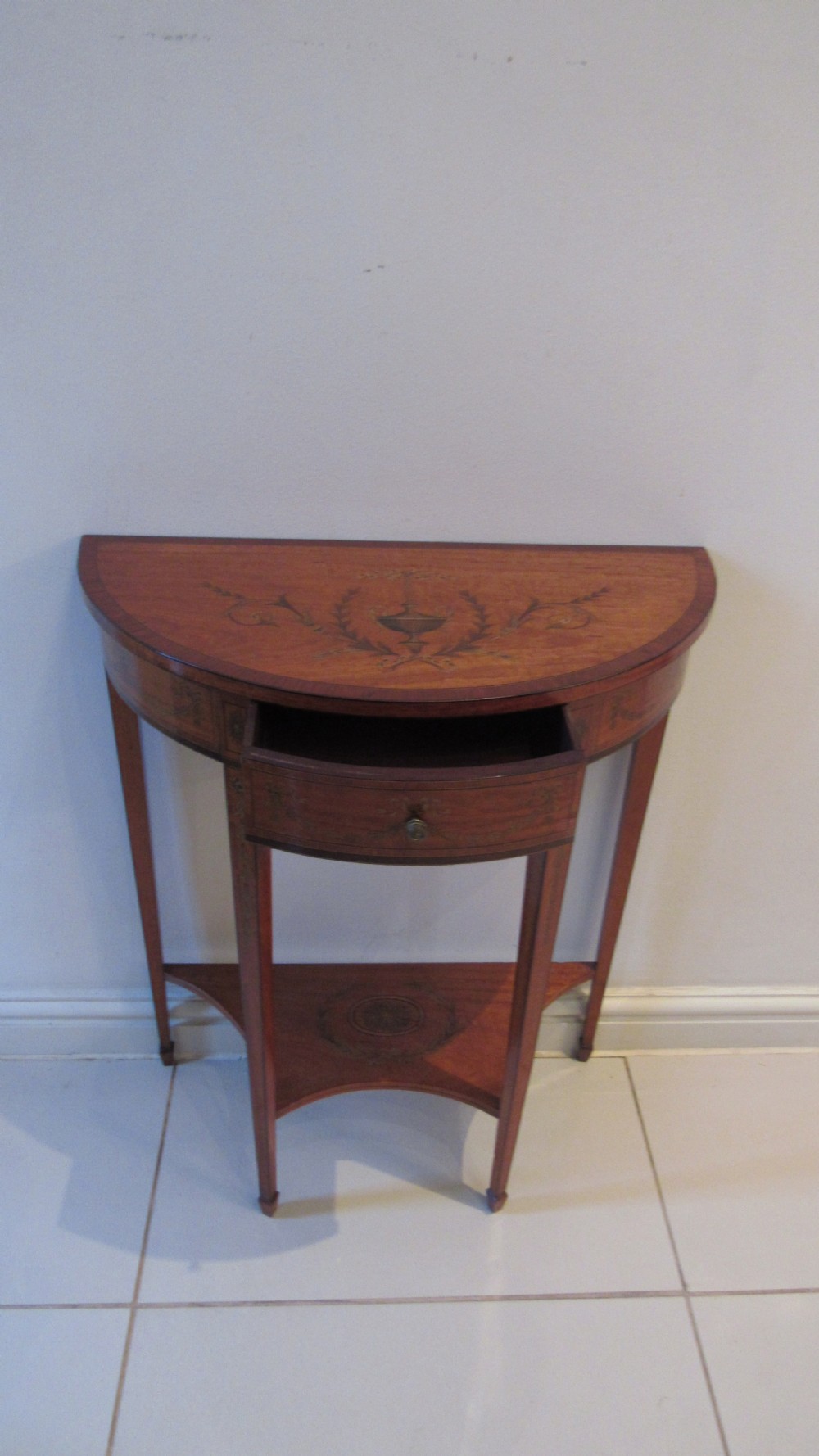 A semi-circular golden satinwood demilune console table featuring urn marquetry inlay, slender tapered legs, and an under-tier shelf. View VII