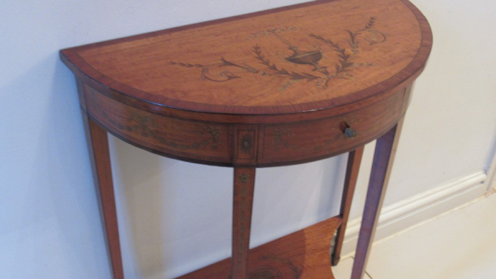 A semi-circular golden satinwood demilune console table featuring urn marquetry inlay, slender tapered legs, and an under-tier shelf. View IX