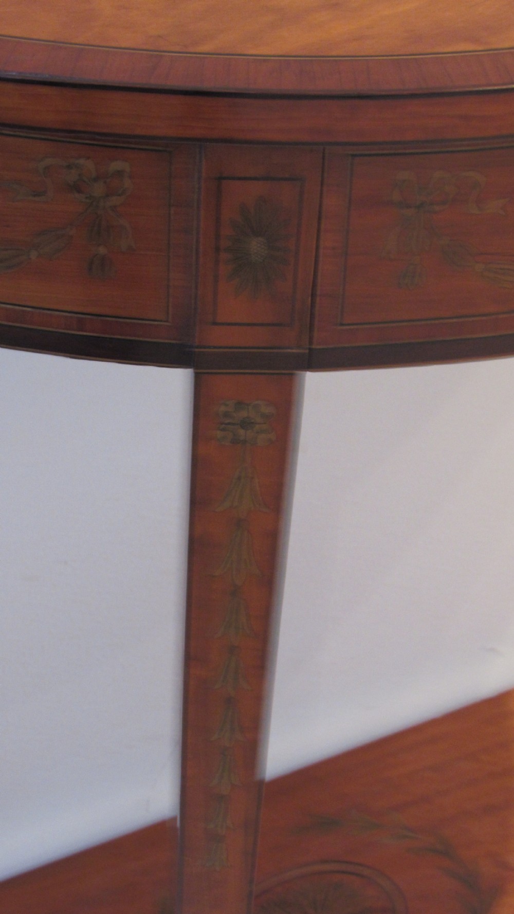 A semi-circular golden satinwood demilune console table featuring urn marquetry inlay, slender tapered legs, and an under-tier shelf. View X