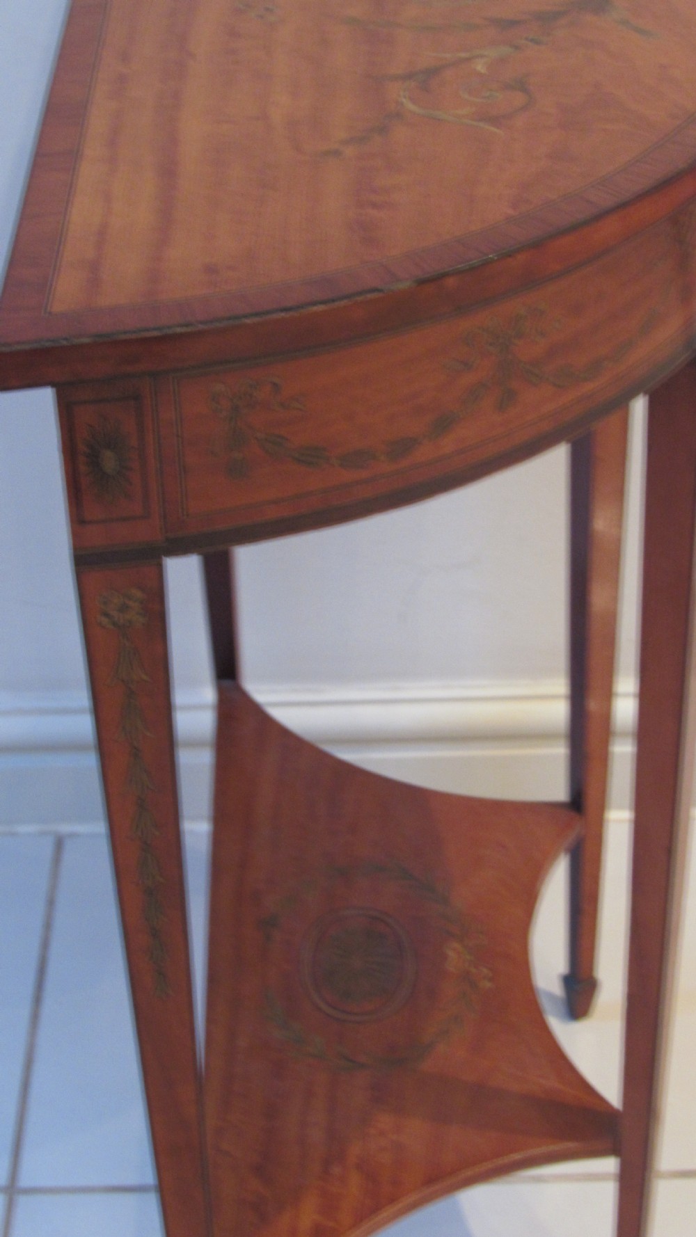 A semi-circular golden satinwood demilune console table featuring urn marquetry inlay, slender tapered legs, and an under-tier shelf. View XI