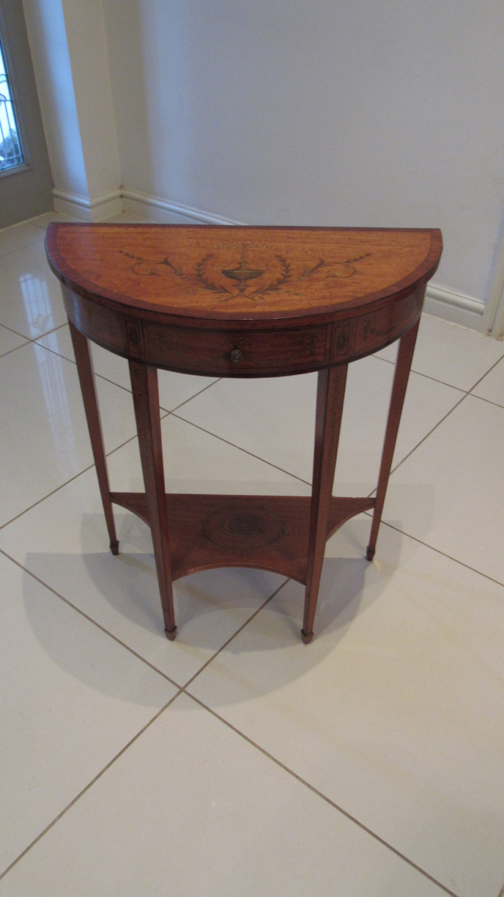 A semi-circular golden satinwood demilune console table featuring urn marquetry inlay, slender tapered legs, and an under-tier shelf. View XIII