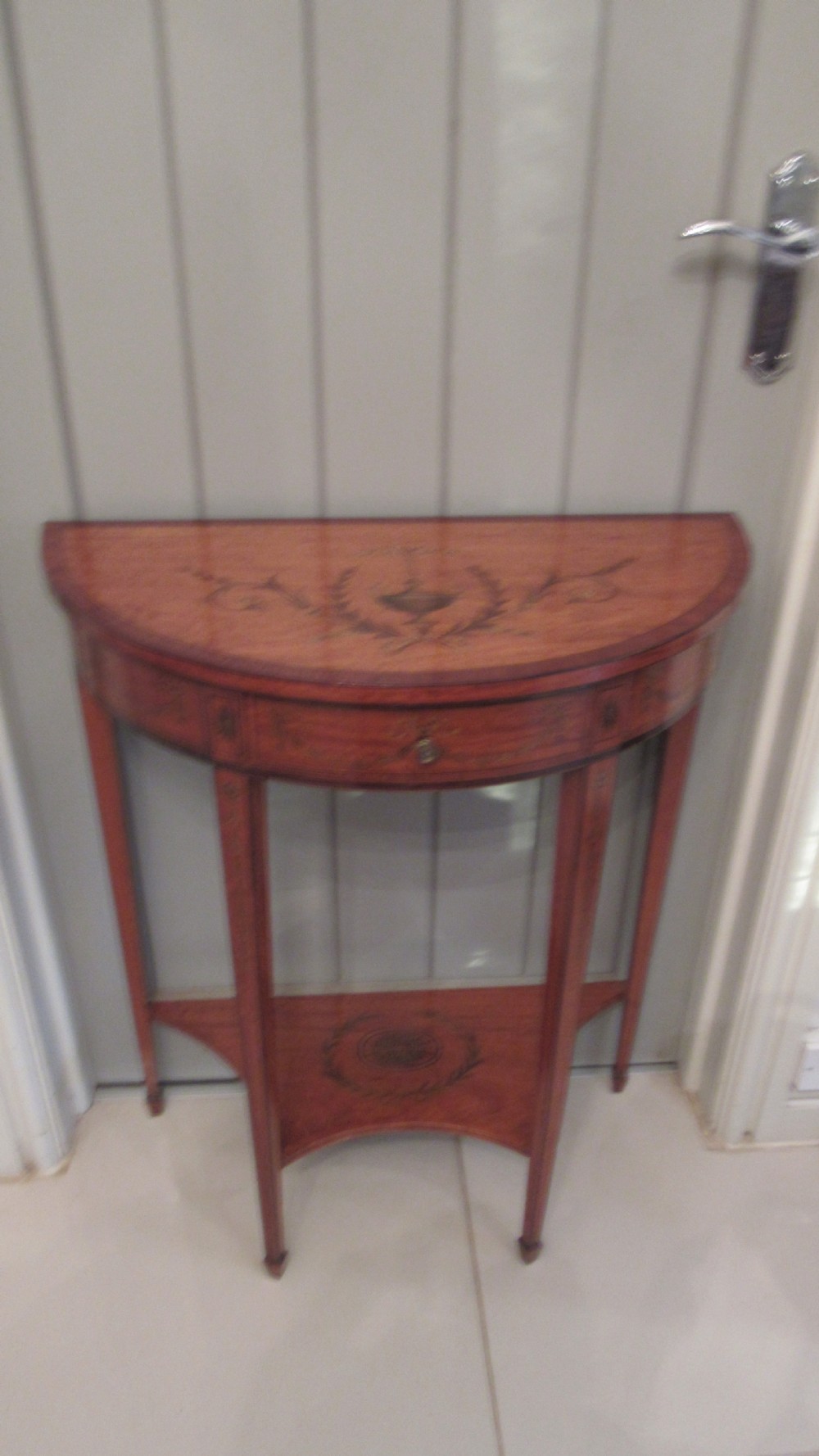 A semi-circular golden satinwood demilune console table featuring urn marquetry inlay, slender tapered legs, and an under-tier shelf. View XV