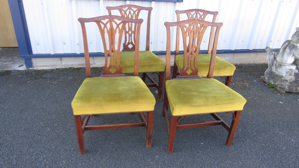 Set of four Georgian mahogany dining chairs featuring carved pierced splats and green velvet upholstered seats.