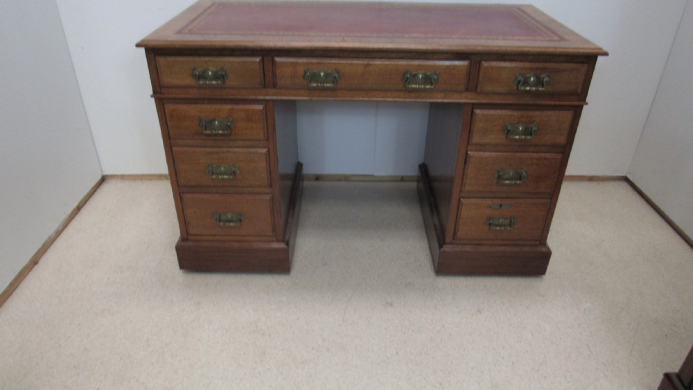 A red walnut pedestal desk featuring a gold-tooled red leather insert writing top, twin drawer pedestals, and brass drop handles. View II