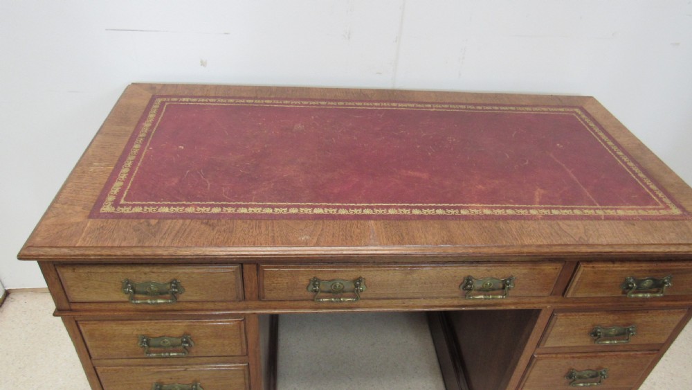 A red walnut pedestal desk featuring a gold-tooled red leather insert writing top, twin drawer pedestals, and brass drop handles. View III