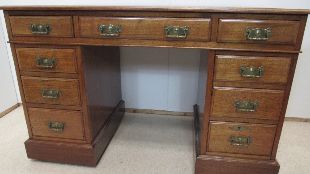 A red walnut pedestal desk featuring a gold-tooled red leather insert writing top, twin drawer pedestals, and brass drop handles. View X