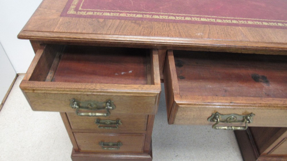 A red walnut pedestal desk featuring a gold-tooled red leather insert writing top, twin drawer pedestals, and brass drop handles. View XIII