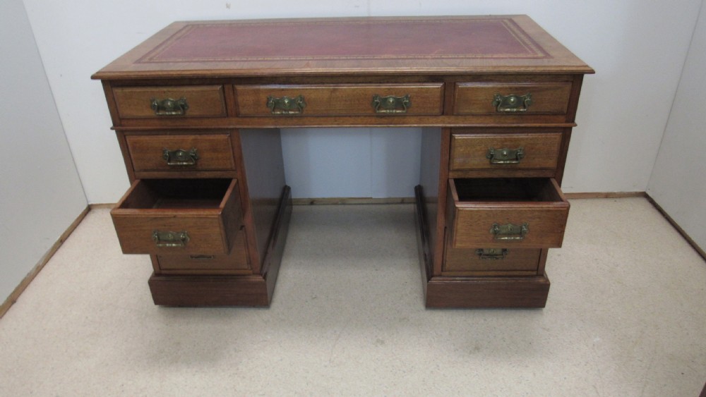 A red walnut pedestal desk featuring a gold-tooled red leather insert writing top, twin drawer pedestals, and brass drop handles. View XIV