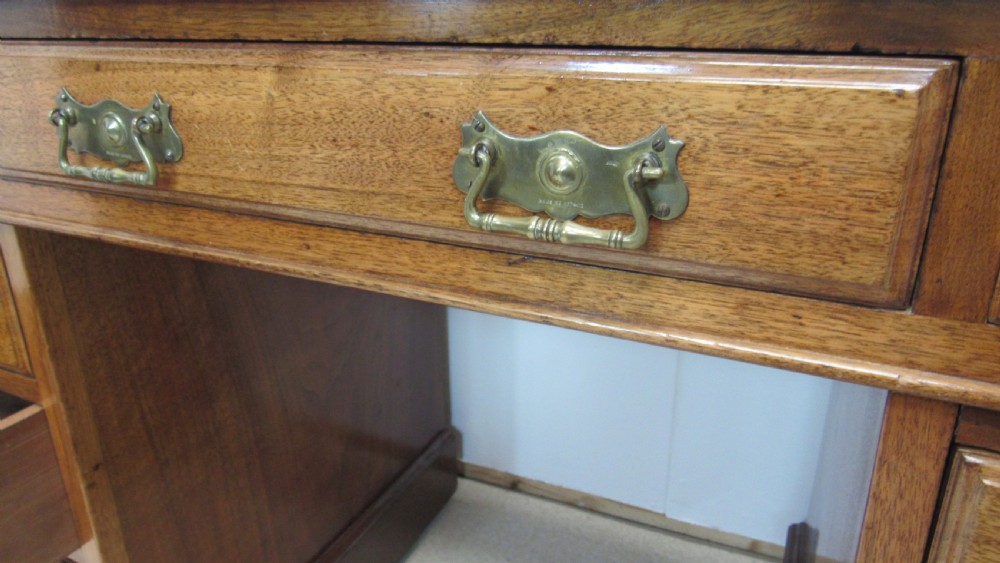 A red walnut pedestal desk featuring a gold-tooled red leather insert writing top, twin drawer pedestals, and brass drop handles. View XVI