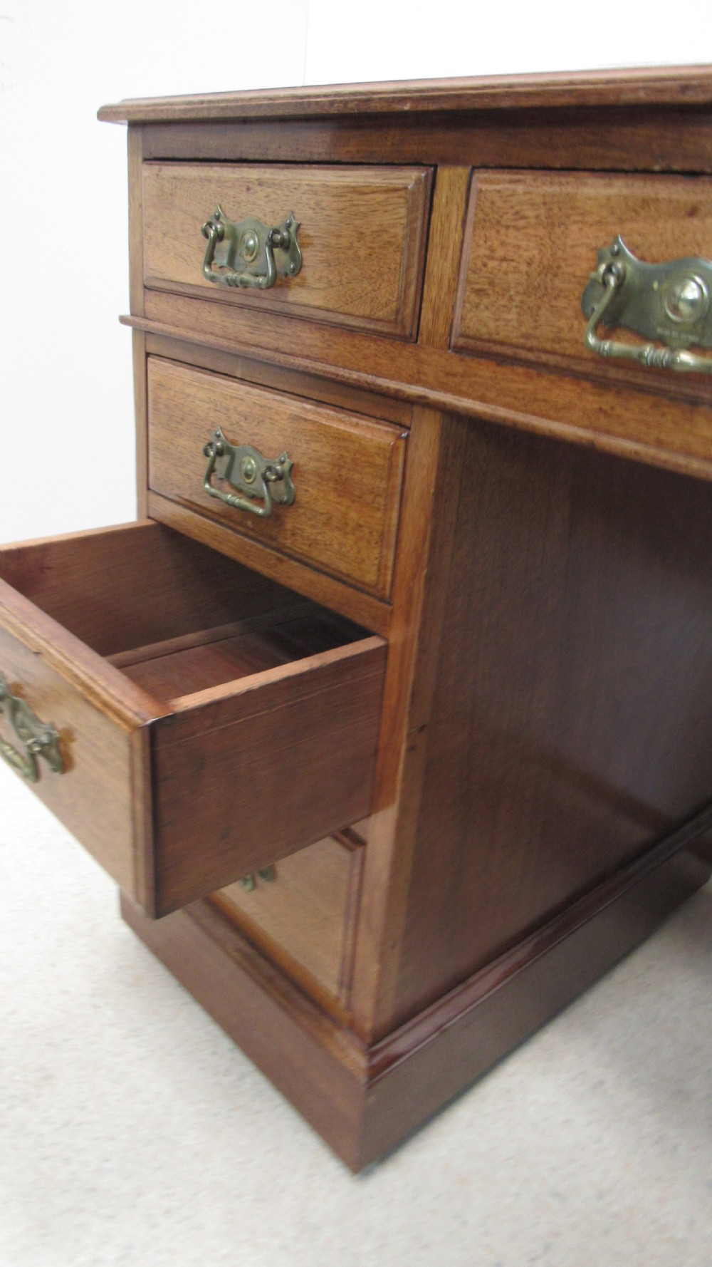 A red walnut pedestal desk featuring a gold-tooled red leather insert writing top, twin drawer pedestals, and brass drop handles. View XVII