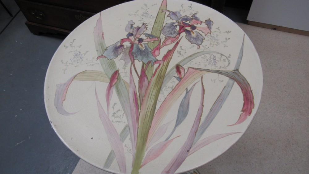 A circular Art Nouveau pottery table featuring a hand-painted floral iris design on a cream-glazed top supported by a sculpted pedestal base. View XX