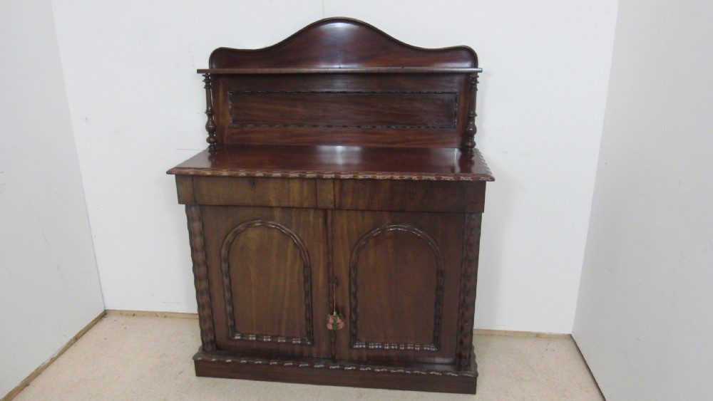 A Victorian mahogany chiffonier featuring an upper gallery shelf with turned side supports above a two-door lower cabinet with arched moulded panels. View V