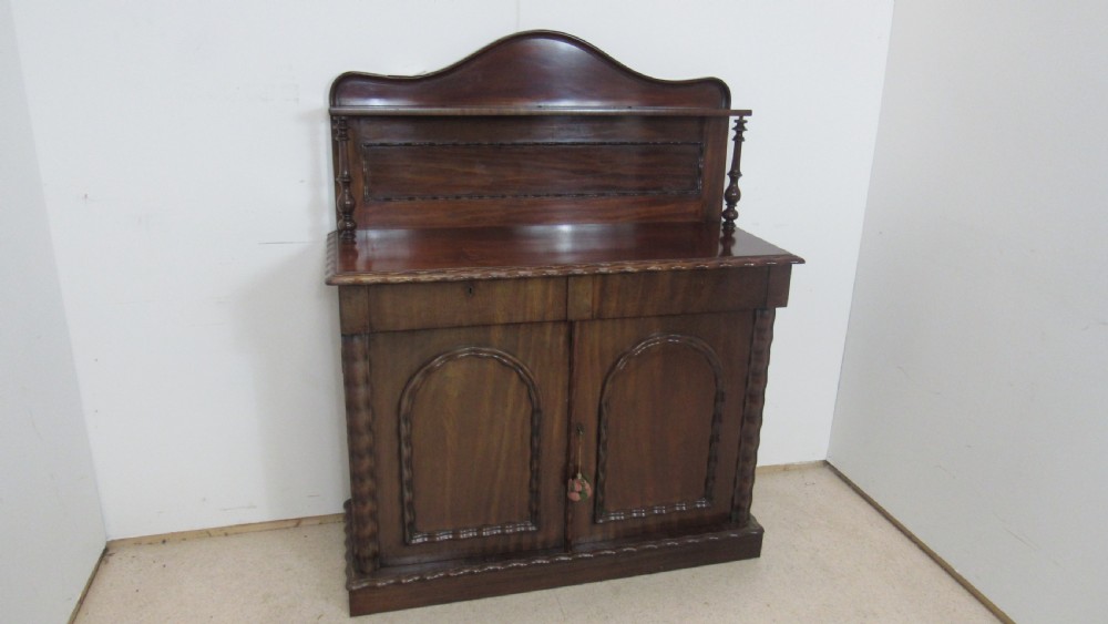 A Victorian mahogany chiffonier featuring an upper gallery shelf with turned side supports above a two-door lower cabinet with arched moulded panels. View VII
