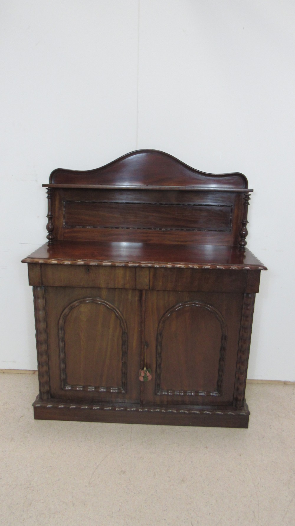 A Victorian mahogany chiffonier featuring an upper gallery shelf with turned side supports above a two-door lower cabinet with arched moulded panels. View XVII