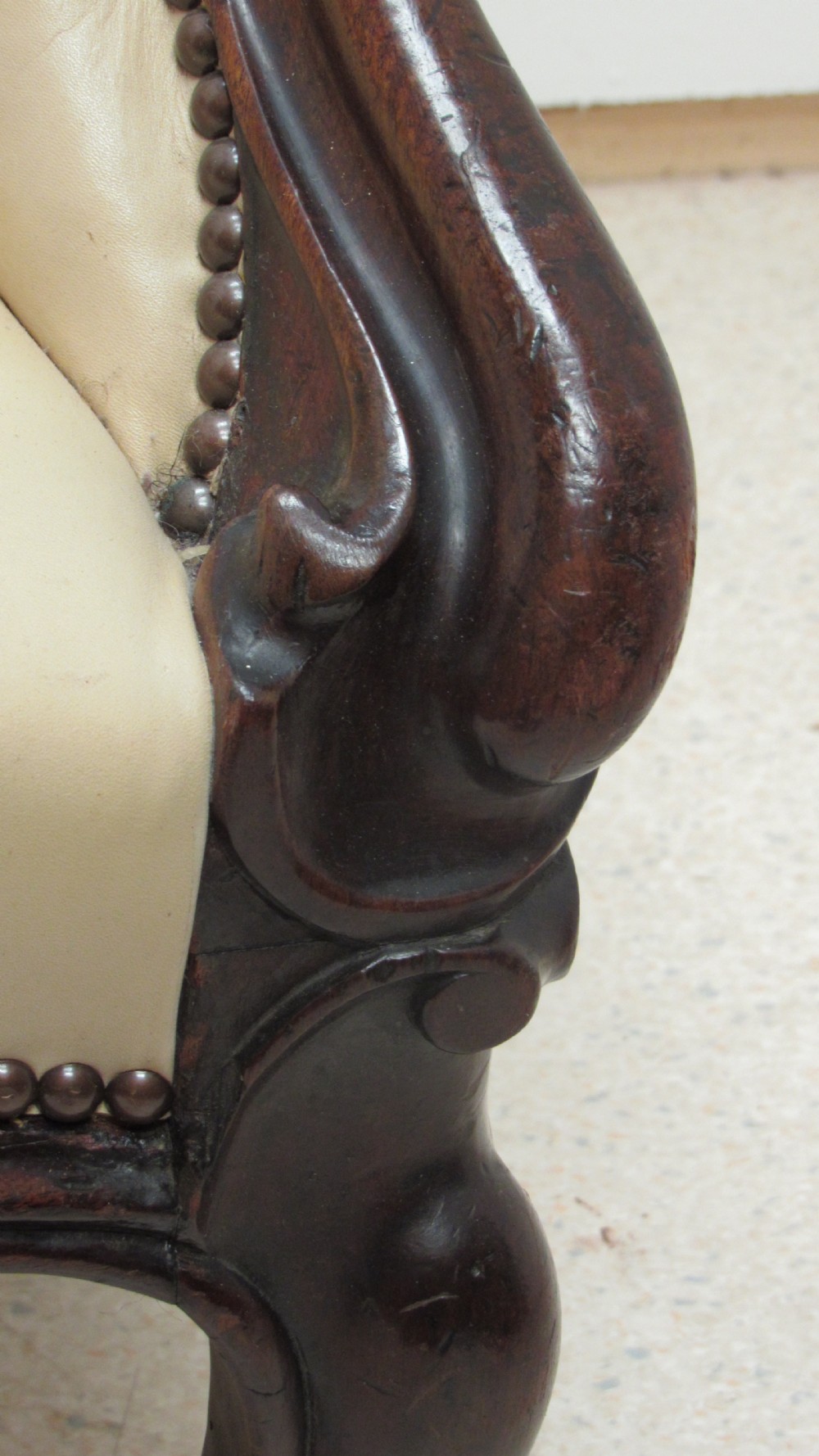 A Victorian library armchair with deep-buttoned cream leather upholstery, a carved dark mahogany frame, padded armrests, and cabriole front legs with brass castors. View V