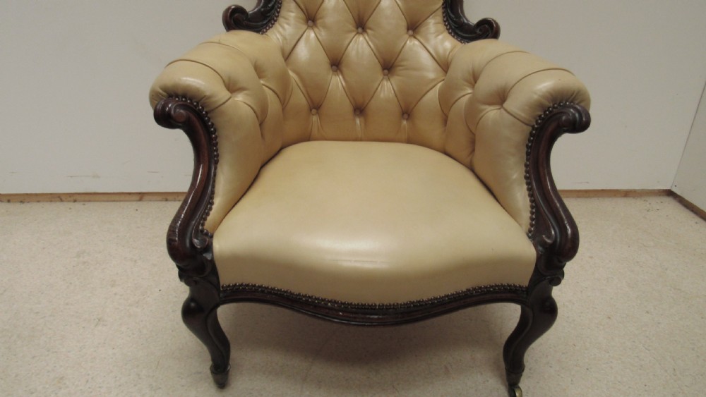 A Victorian library armchair with deep-buttoned cream leather upholstery, a carved dark mahogany frame, padded armrests, and cabriole front legs with brass castors. View VIII