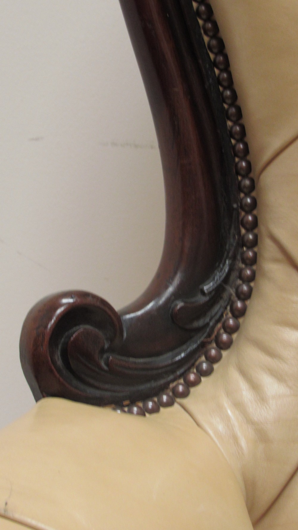 A Victorian library armchair with deep-buttoned cream leather upholstery, a carved dark mahogany frame, padded armrests, and cabriole front legs with brass castors. View IX