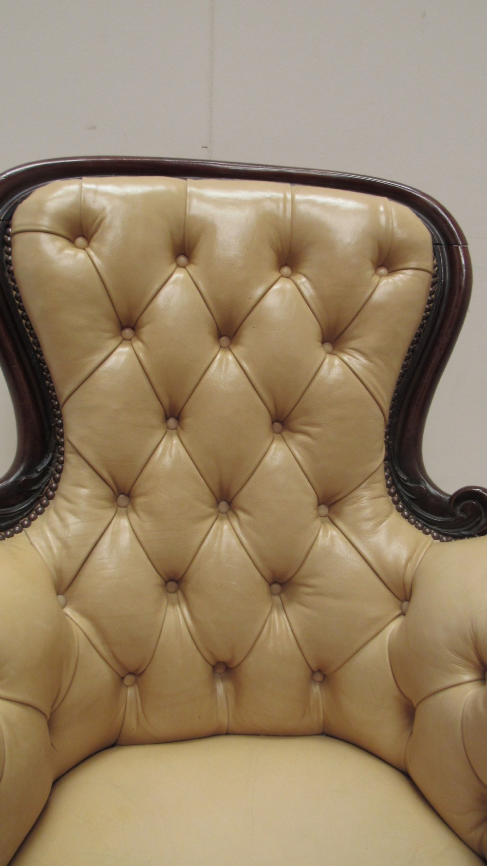 A Victorian library armchair with deep-buttoned cream leather upholstery, a carved dark mahogany frame, padded armrests, and cabriole front legs with brass castors. View XI