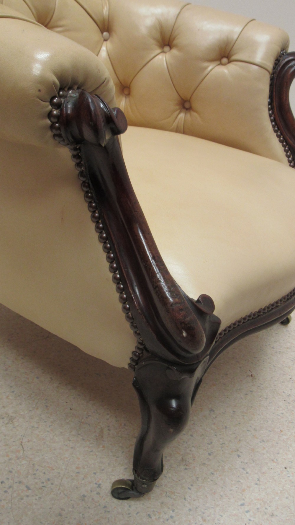 A Victorian library armchair with deep-buttoned cream leather upholstery, a carved dark mahogany frame, padded armrests, and cabriole front legs with brass castors. View XIII