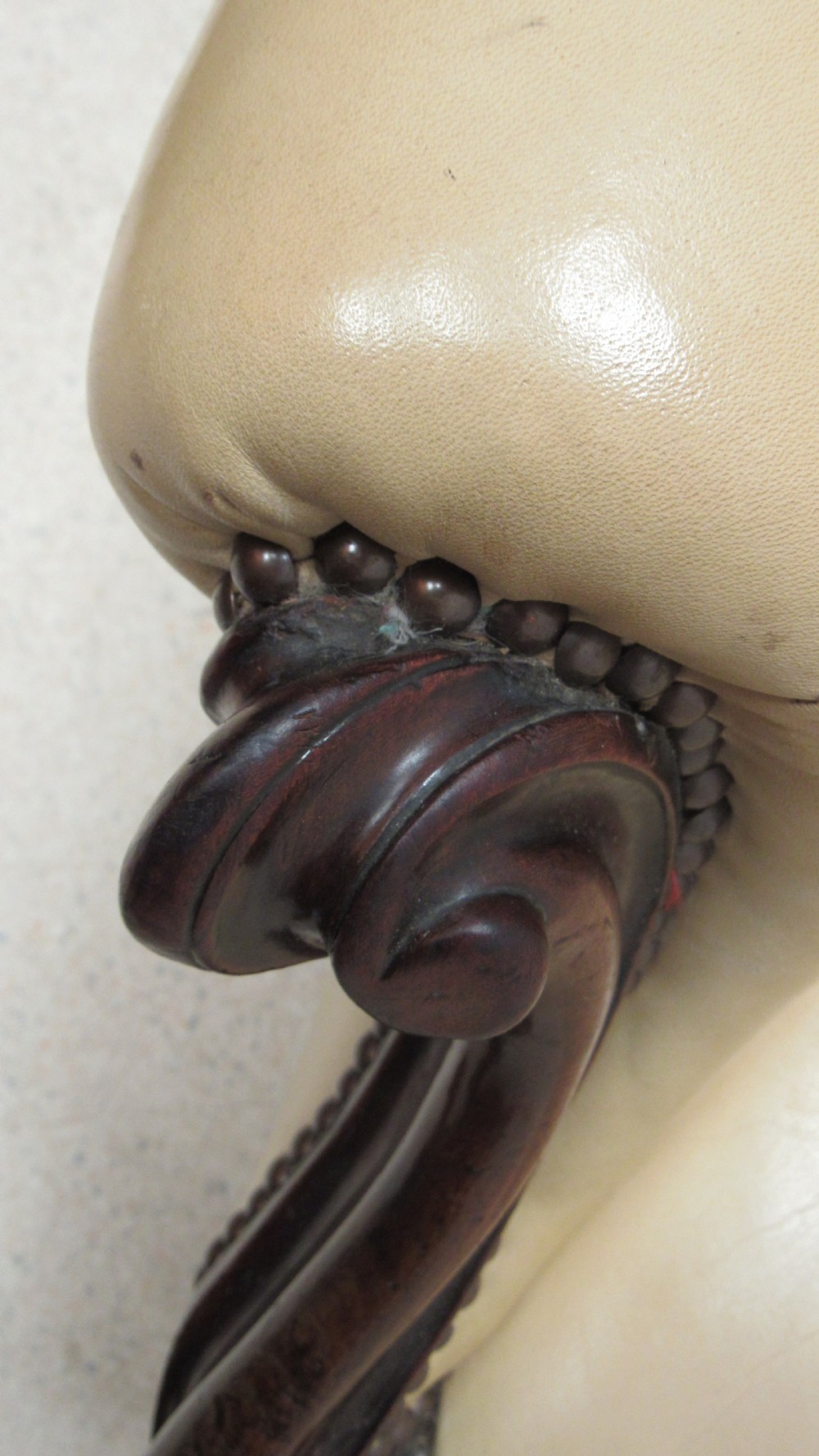 A Victorian library armchair with deep-buttoned cream leather upholstery, a carved dark mahogany frame, padded armrests, and cabriole front legs with brass castors. View XIV