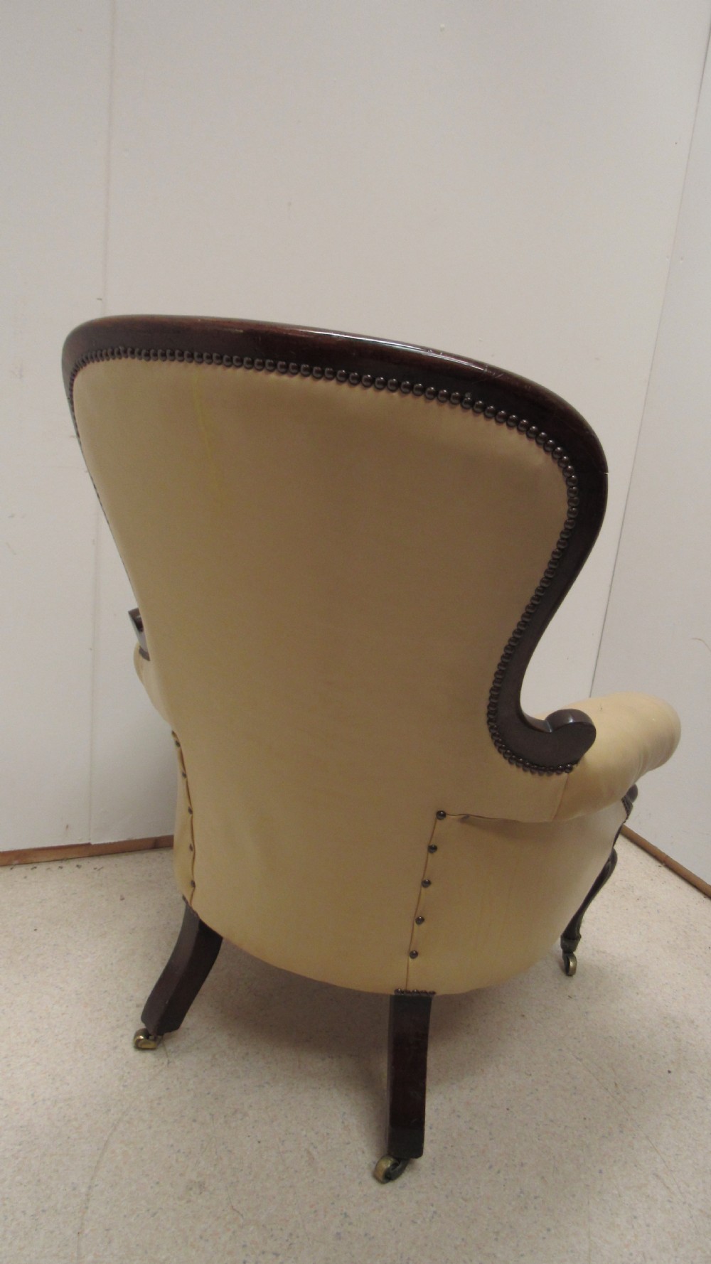 A Victorian library armchair with deep-buttoned cream leather upholstery, a carved dark mahogany frame, padded armrests, and cabriole front legs with brass castors. View XVI