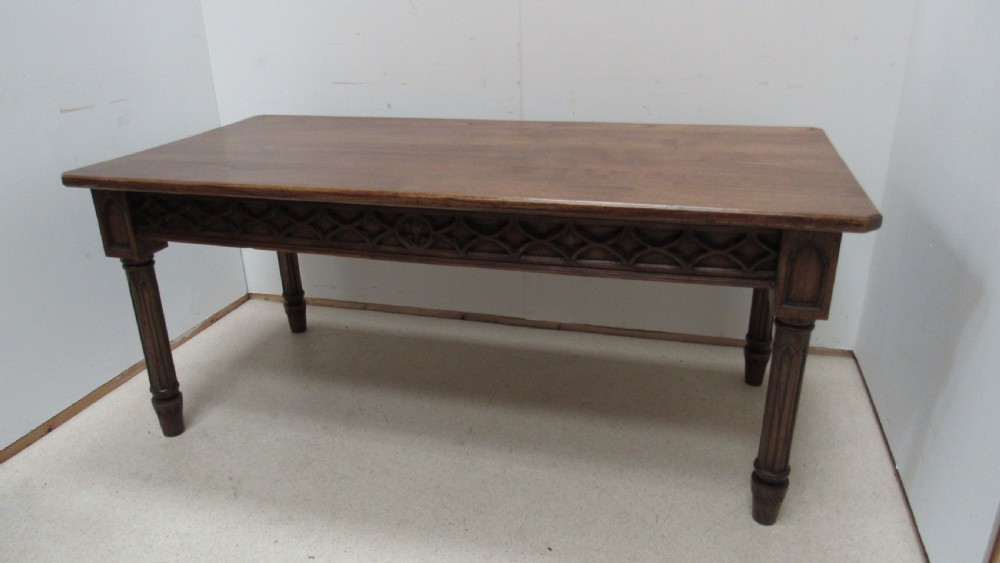 A rectangular solid oak refectory table featuring carved Gothic blind tracery along the frieze and turned column legs.