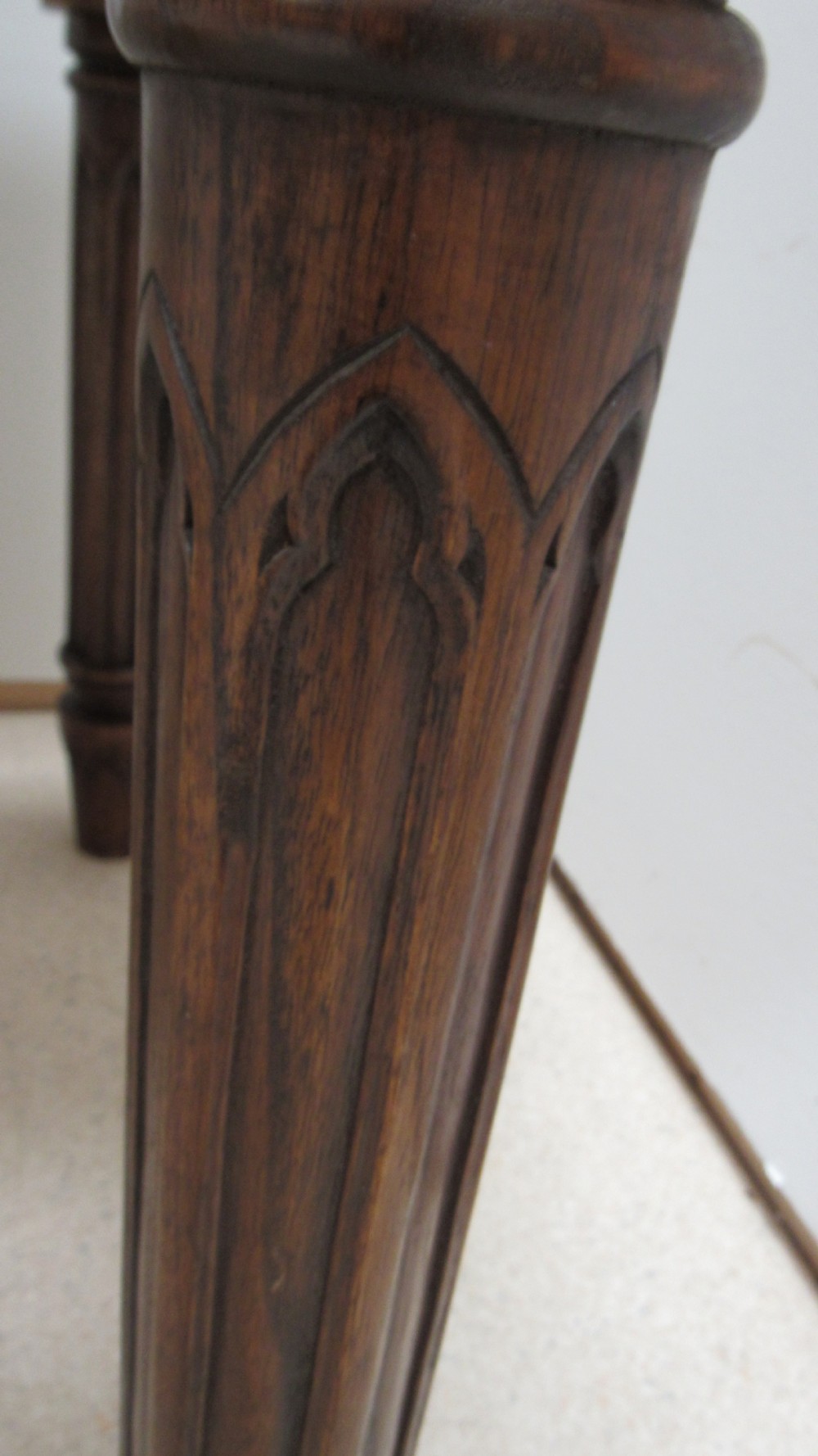 A rectangular solid oak refectory table featuring carved Gothic blind tracery along the frieze and turned column legs. View V