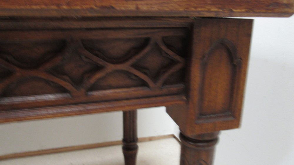 A rectangular solid oak refectory table featuring carved Gothic blind tracery along the frieze and turned column legs. View VIII