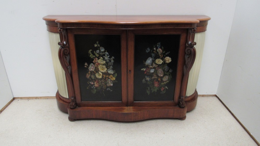 A nineteenth-century dark wood side cabinet featuring two central black door panels decorated with floral arrangements, framed by carved scroll supports and curved pleated side sections.
