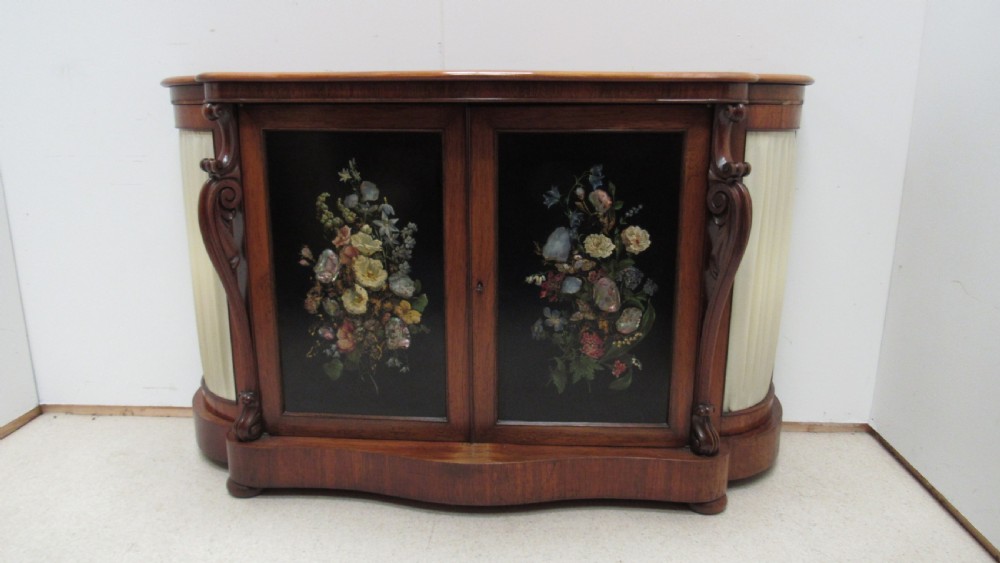A nineteenth-century dark wood side cabinet featuring two central black door panels decorated with floral arrangements, framed by carved scroll supports and curved pleated side sections. View II