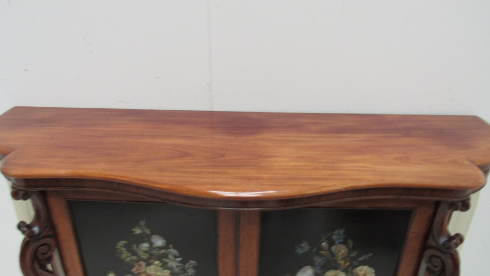 A nineteenth-century dark wood side cabinet featuring two central black door panels decorated with floral arrangements, framed by carved scroll supports and curved pleated side sections. View III