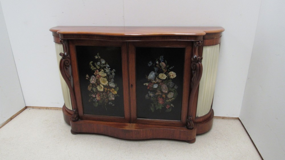A nineteenth-century dark wood side cabinet featuring two central black door panels decorated with floral arrangements, framed by carved scroll supports and curved pleated side sections. View XI