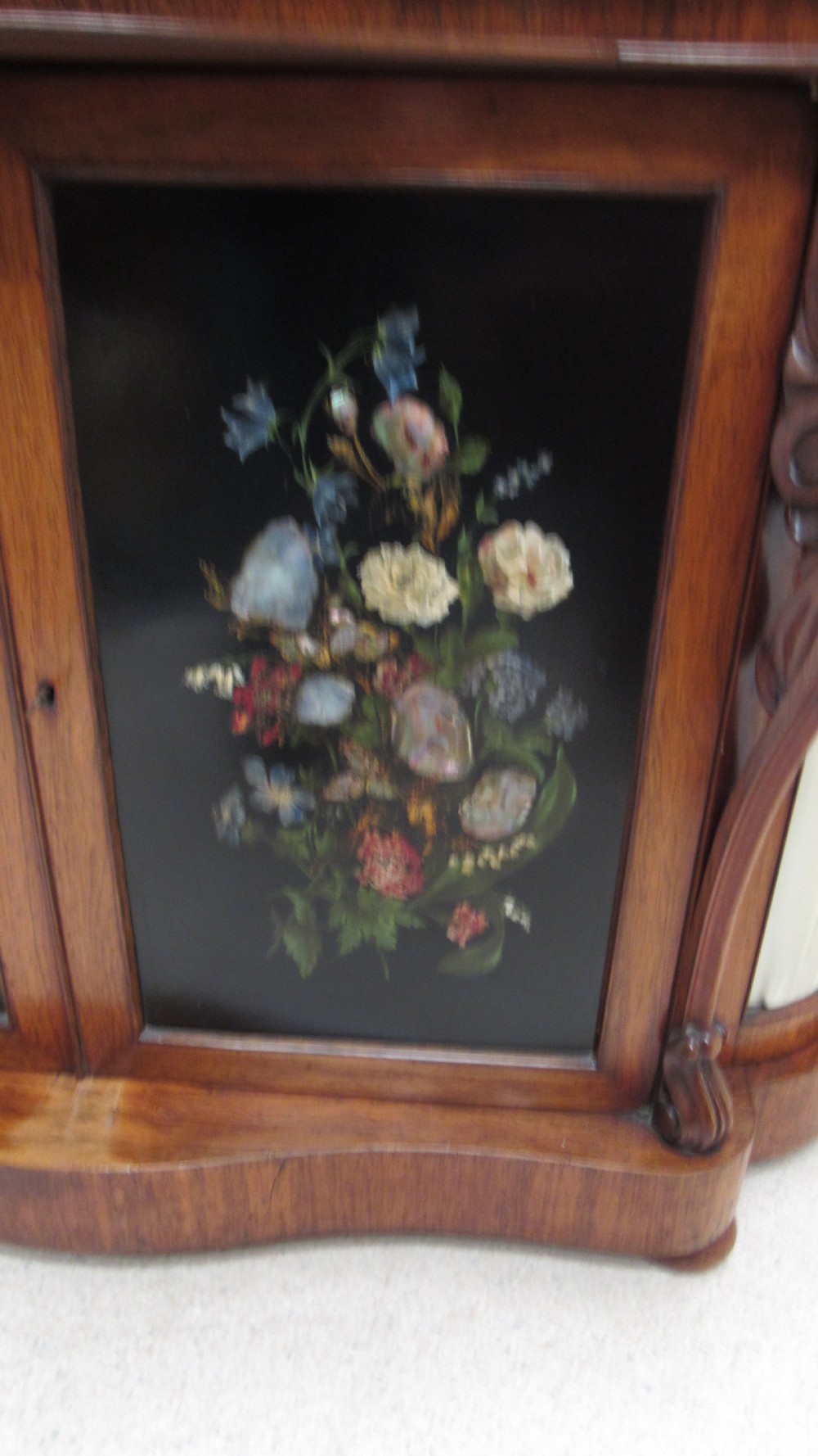 A nineteenth-century dark wood side cabinet featuring two central black door panels decorated with floral arrangements, framed by carved scroll supports and curved pleated side sections. View XIII