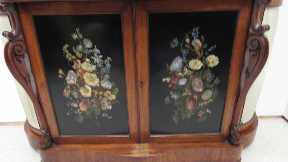 A nineteenth-century dark wood side cabinet featuring two central black door panels decorated with floral arrangements, framed by carved scroll supports and curved pleated side sections. View XIV
