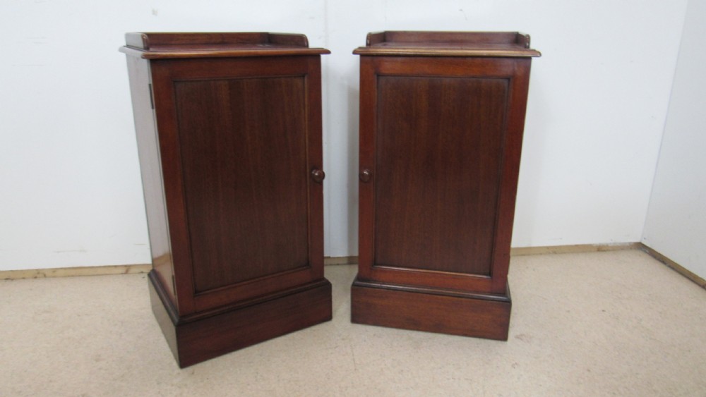 A pair of antique mahogany pot cupboards featuring three-sided gallery tops, single panelled doors with wooden knobs, and solid plinth bases.
