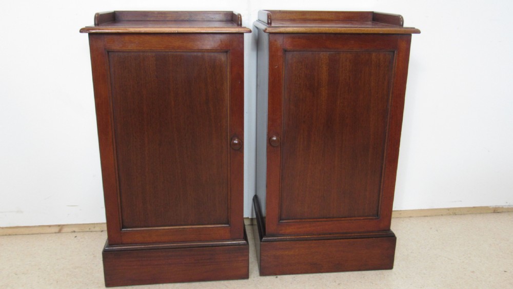 A pair of antique mahogany pot cupboards featuring three-sided gallery tops, single panelled doors with wooden knobs, and solid plinth bases. View V