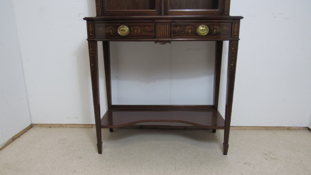 An Edwardian dark mahogany display cabinet featuring a swan-neck pediment, delicate satinwood floral marquetry, two glazed upper doors, drawers with brass handles, and tapered legs with an undertier shelf. View II